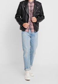 Czarna skórzana kurtka motocyklowa z pagonami, kieszenie na zamek, różowa koszula w kratę pod spodem, jasnoniebieskie dżinsy i białe wysokie trampki.