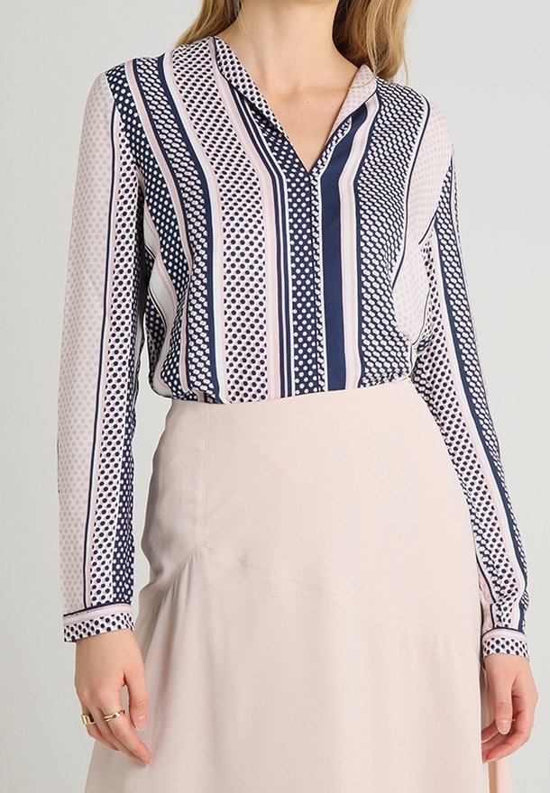Femme portant un chemisier à manches longues avec des rayures verticales bleu marine et blanches et des pois, associé à une jupe beige clair.
