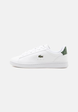 Baskets basses blanches avec logo crocodile vert sur le côté et languette de talon à motif vert, lacets blancs et semelle en caoutchouc plate.