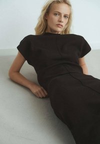 Vestido midi de punto negro con mangas cortas, que presenta un detalle de costura en el frente y un ajuste relajado, colocado sobre un fondo claro.