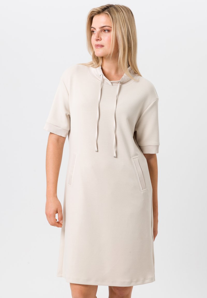 Robe beige clair en tissu doux, dotée d'une capuche, de manches courtes et de deux poches avant avec des coutures décoratives.