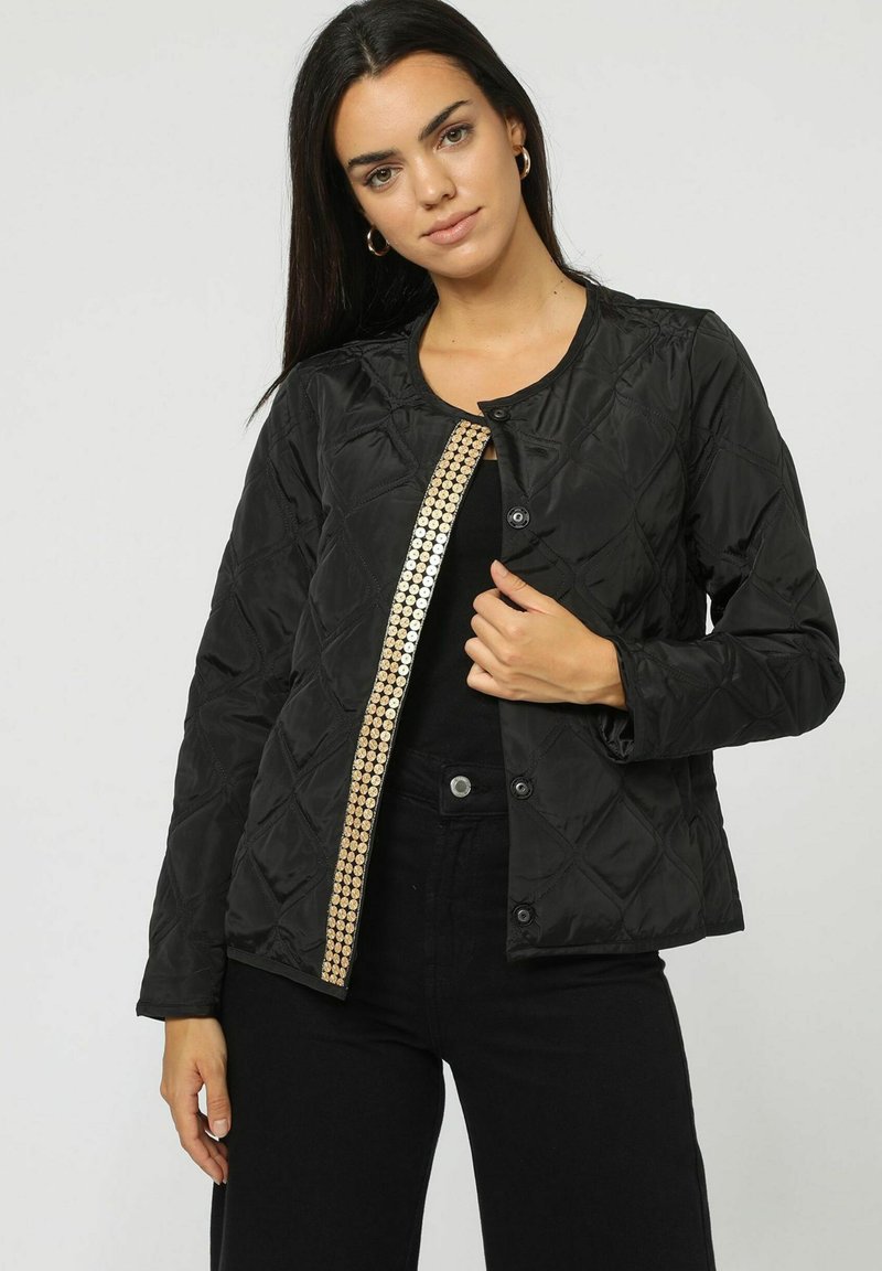 Chaqueta negra acolchada con un detalle de lentejuelas doradas a lo largo de la apertura frontal. Presenta un cuello redondo y cierres de botones.