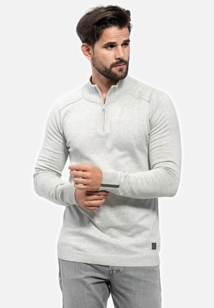 Cárdigan gris claro con cremallera, confeccionado en un suave material de punto, que cuenta con un alto cuello, puños acanalados y una pequeña etiqueta de marca en el dobladillo.