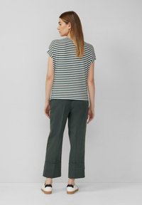 Gestreepte top met korte mouwen in navy en crème, gecombineerd met groene brede broek met een omgevouwen zoom, en witte schoenen met zwarte accenten.