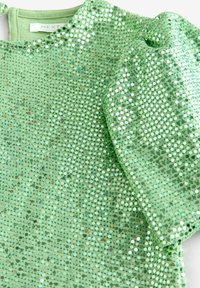 Top en sequins verts avec une surface texturée, featuring des sequins ronds et réfléchissants disposés de manière rapprochée, et des manches courtes bouffantes.