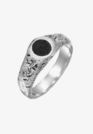 Bague en argent présentant un design texturé et rugged avec une grande pierre noire circulaire au centre, mettant en valeur un mélange de finitions polies et mates.