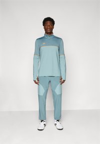 Ropa deportiva de color azul claro con parte superior de media cremallera y parte inferior a juego. La tela texturizada presenta acentos naranjas y detalles en panel.