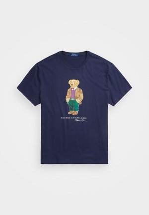 Marineblauw katoen T-shirt met een gedetailleerd geborduurd beer in een blazer, met een vest en broek, naast de tekst "POLO BEAR by RALPH LAUREN".