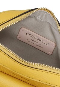 Žlutá kožená peněženka uvnitř s lehkou látkovou podšívkou. Zapínání na zip a štítek s nápisem "Coccinelle Authentic Italian Leather."