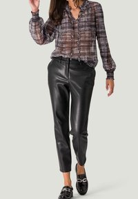 Blouse à carreaux translucide dans des teintes grises, marron et noires ; pantalons taper en simili cuir noir ; mocassins noirs brillants avec des accents argentés.