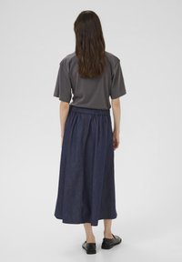 Top gri cu mâneci scurte și fustă lungă din denim bleu închis, cu talie elastică, asociată cu pantofi negri, fără toc. Design minimalist, fără modele vizibile.