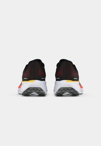 Zapatillas de correr negras con acentos en rojo y amarillo, con una parte superior texturizada, un collar acolchado y una mediasuela blanca con una suela de goma con patrón.