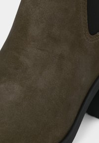 Bottines en daim vert olive avec une texture lisse, bout rond, panneau latéral élastique et petit talon en caoutchouc noir.