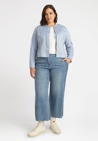 Chaqueta de cuero azul claro con cuello redondo, botones a presión y bolsillos laterales, combinada con jeans de pierna ancha y zapatillas color crema.
