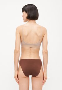 Beige bralette en bruine bikini-broekjes gemaakt van gladde rekbare stof, met dunne bandjes en een minimalistisch ontwerp.