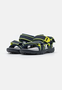 Sport sandals med marineblå stoffstropper med neon gule detaljer, en polstret såle, og en robust svart gummisåle.