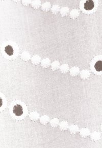 Tissu blanc avec des œillets circulaires brodés et de petits motifs floraux disposés en lignes horizontales incurvées.
