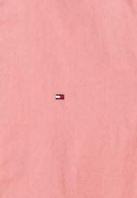 Tessuto rosa con una trama liscia, dotato di un piccolo logo rettangolare ricamato al centro in navy, rosso e bianco.