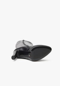Black leather high-heeled boot showing a smooth texture, pointed toe, and a rounded heel. Features a zipper and subtle design accents.
