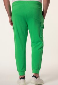Groene cargobroek met een elastische tailleband. Beschikt over zij- en achterzakken. Stof heeft een gladde textuur. De boorden zitten nauw om de enkels.