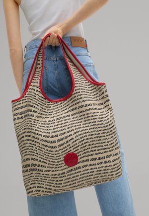 Beige tote bag med sort "JOOP!JEANS" tekst, rød kant og et cirkulært logo patch. Blødt materiale, rummelig design og rummelige hanke.
