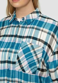Camicia button-up a quadri blu chiaro con diverse tonalità di blu, nero e bianco, dotata di taschino sul petto e colletto classico.
