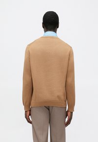 Brunstickad tröja med rund halsringning och ribbade muddar, kombinerad med grå byxor. Tyget verkar mjukt med en slät textur.