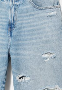 Jean denim bleu clair avec des déchirures usées sur la cuisse et près du genou, poche avant visible et détails de couture jaunes.