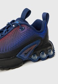 Baskets en maille marine avec un design dégradé violet-bleu, semelle noire, rembourrage Air proéminent et accents texturés près du logo.