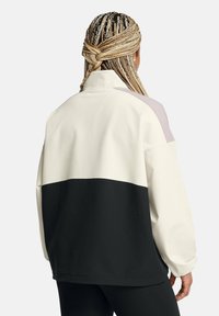 Color-blocked sweatshirt with a cream upper section, lavender shoulder accents, and a black lower section. Soft material and relaxed fit.