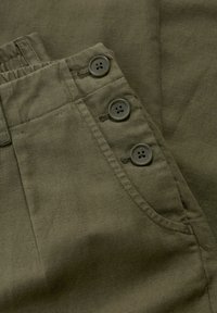 Olivgrön byxor i strukturerad tyg, med en ficka som har tre grå knappar och synliga sömdetaljer.