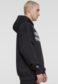 Fekete kapucnis pulóver pamut keverék anyagból. Elöl kenguruzseb, hímzett "New Balance" logó és oldal grafikai részlet található az ujjon.