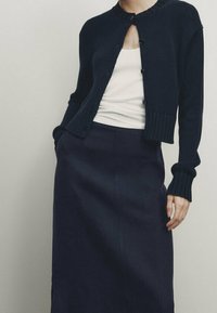 Merenneidon neulepusero pyöreällä kauluksella, napitus edessä ja resorikätkät, yhdistettynä samasta merenneidon väristä hameeseen, jossa on sileä pinta.