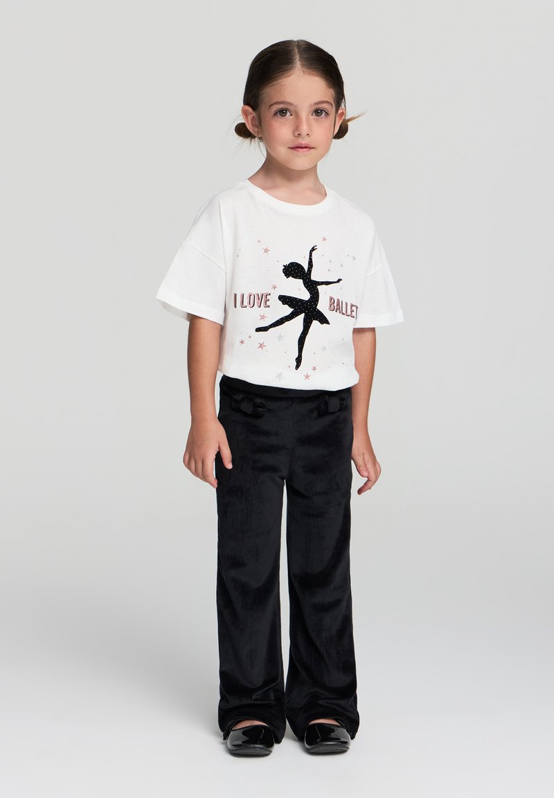 Biała bawełniana koszulka z czarnym graficznym motywem tancerza i napisem "KOCHAM BALLET". Czarne sztruksowe spodnie o miękkiej strukturze i szerokich nogawkach. Czarne buty.