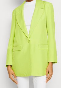 Marynarka w kolorze limonkowej zieleni z gładkiego materiału, wyposażona w pojedyncze zapięcie na guzik, dwie przednie kieszenie oraz klasyczny kołnierz.