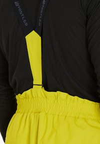 Gula vattentåliga overaller med elastisk midja och justerbara svarta hängslen. Tyget är slätt och designen är funktionell för utomhusbruk.