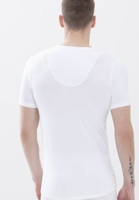 T-shirt bianco aderente a maniche corte realizzato in tessuto leggero con una texture liscia. Presenta un collo arrotondato e un discreto dettaglio di design sul retro.