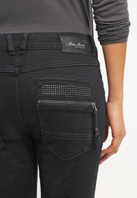 Černé džíny z denimu s přiléhavým střihem. Mezi funkce patří zadní kapsa se zdobením ve tvaru hřebíčků a zipová kapsa na pravé straně.