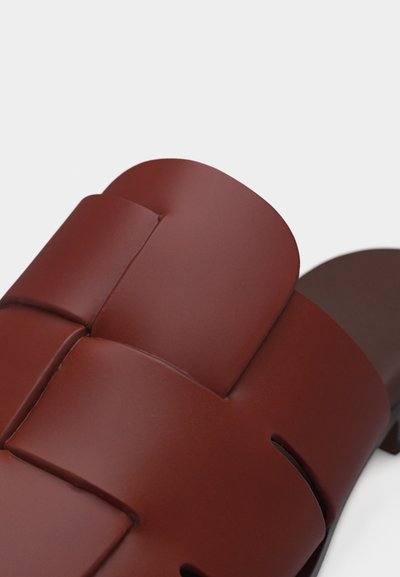 Κοντινή λήψη καφέ δερμάτινου σανδαλιού slide με φ αρδιές, επενδεδυμένες λουράκια και σκουρό καφέ επίπεδη σόλα.