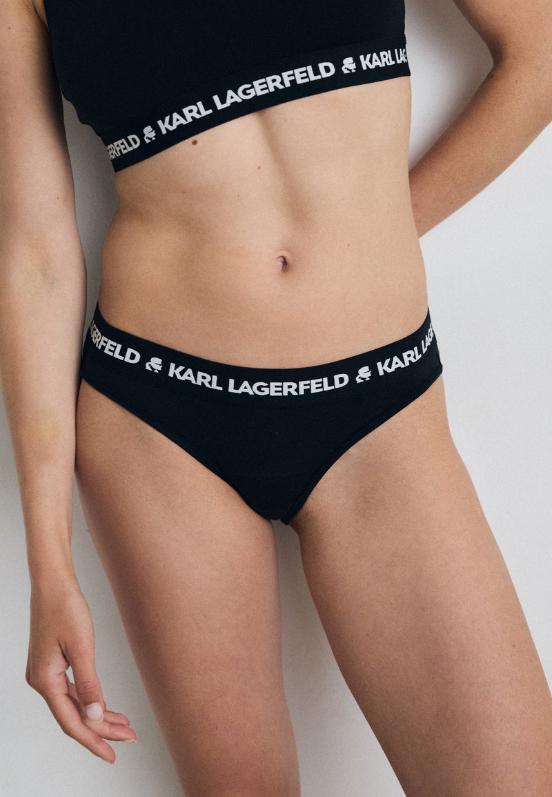 Perizoma di cotone nero con gamba alta, caratterizzato da una banda bianca a contrasto con il marchio "KARL LAGERFELD" lungo la vita.