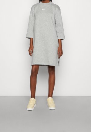 Szara sukienka z dresu z rękawami do łokcia, ozdobiona subtelnym białym logo na piersi. Zestawiona z jasnżółtymi sneakersami.