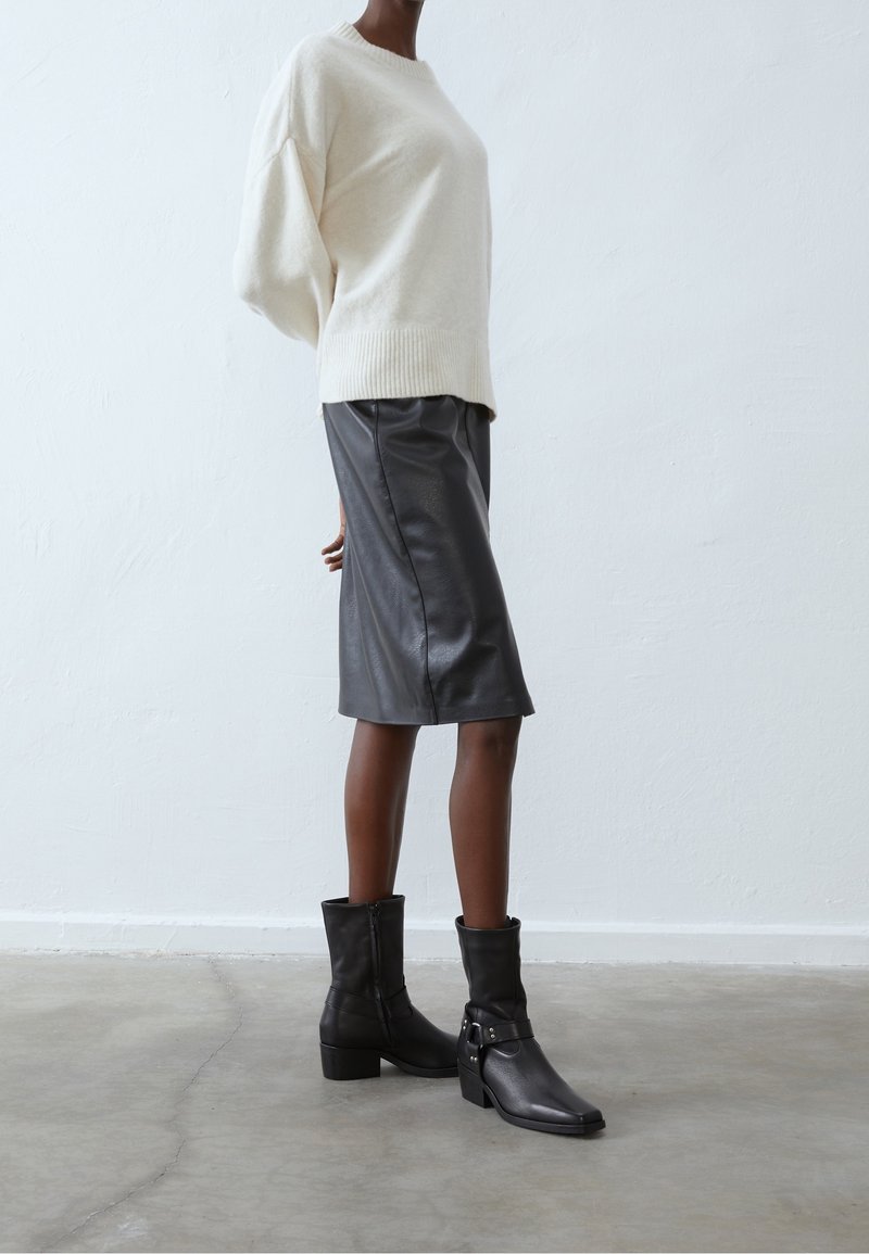 Suwakowany sweterek w kolorze kości słoniowej z ribbowym wykończeniem, połączony z czarną skórzaną spódnicą ołówkową. Czarne botki za kostkę z detalami w postaci klamry i kwadratowym noskiem.