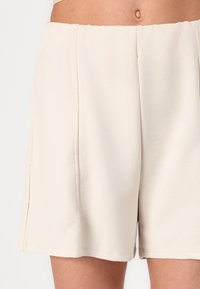 Shorts de couleur crème en tissu lisse, avec des poches latérales, une coupe droite et une taille élastique pour plus de confort.