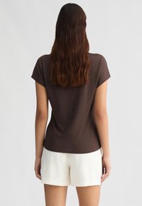 Top corto marrone a maniche corte con vestibilità rilassata, texture liscia e orlo arrotondato, abbinato a pantaloni corti bianchi con texture.