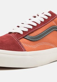 Punaiset ja oranssit kankaiset ja mokkaiset lenkkarit valkoisilla nauhoilla, mustalla nahkaviivalla ja teksturoidulla valkoisella pohjalla. Ompeleet korostavat muotoiluelementtejä.