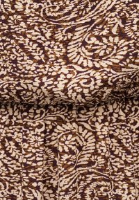 Ύφασμα με περίπλοκα μοτίβα από καφέ και μπεζ λουλούδια και φύλλα, παρουσιάζοντας λεπτομέρειες υφής και ραφής.