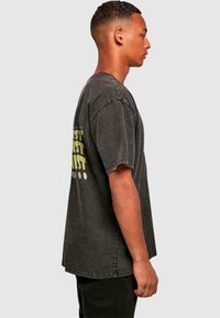 Graues Baumwoll-T-Shirt mit lockerer Passform, das auf der Rückseite mit einem grafischen Druck in Gelb und Weiß versehen ist. Kurze Ärmel und Rohschnittdetails.