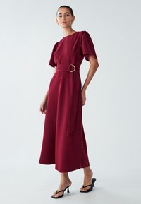 Burgundijas midi kleita ar īsām puff piedurknēm, josta ar zelta gredzenu un taisnu siluetu. Gluda auduma, minimālisma stila.