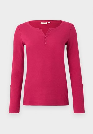 Langärmliges pinkes Oberteil mit gerippter Textur, das eine Henley-Ausschnitt und eine Knopfleiste mit drei Knöpfen aufweist. Enthält Schlitzakzente an den Ärmelenden.