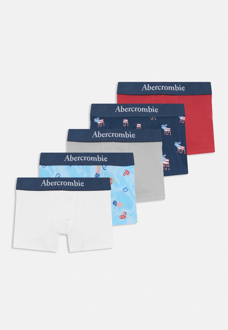 Fem par med gutteboxershorts i forskjellige farger: hvit, lyseblå med mønster, grå, marineblå med design, og rød, hver med marineblå midjebånd.